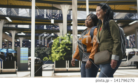 Friends walking together through modern bus terminal while chatting. Passengers carrying backpacks in shuttle station enjoying friendly conversation before departure Friends walking together through modern bus terminal while chatting. Passengers carrying backpacks in shuttle station enjoying friendly conversation before departure 141796270