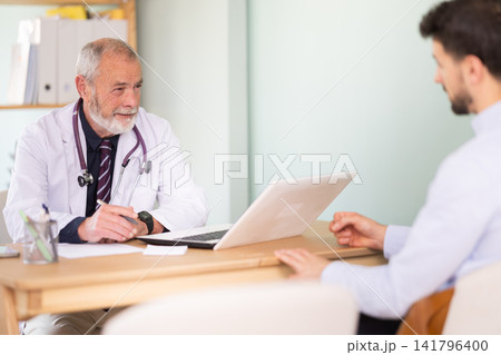 Man client of medical clinic sits opposite mature male doctor and communicates with specialist Man client of medical clinic sits opposite mature male doctor and communicates with specialist 141796400