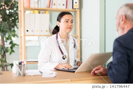 Adult female doctor talking with elderly male patient in medical office 141796447