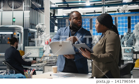 African american engineers team collaborating in a solar panel facility, examining blueprints to guarantee production line infrastructure and sharing ideas for alternative energy. Camera A. African american engineers team collaborating in a solar panel facility, examining blueprints to guarantee production line infrastructure and sharing ideas for alternative energy. Camera A. 141796564