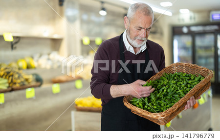 Elderly male placing green peppers in basket on store counter 141796779