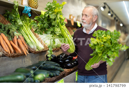 Elderly man chooses celery for purchase in greengrocer shop Elderly man chooses celery for purchase in greengrocer shop 141798799