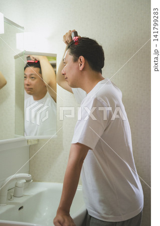 洗面台に向かいスカルプ電気ブラシで頭皮を刺激する40代男性のヘアケア 洗面台に向かいスカルプ電気ブラシで頭皮を刺激する40代男性のヘアケア 141799283