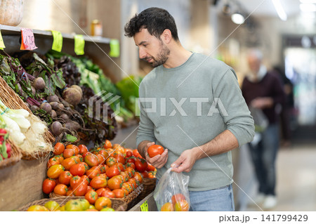 man stands near a counter with fresh tomatoes, he carefully selects them man stands near a counter with fresh tomatoes, he carefully selects them 141799429