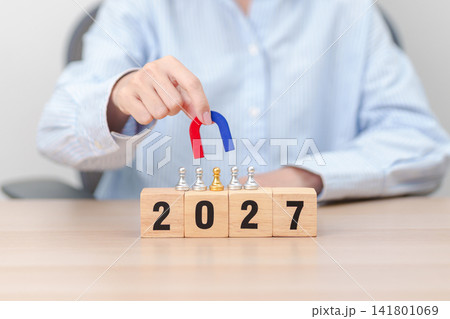 hand holding magnet and pulling man chess figure from the crowd employee with 2027 Year block. Human resource management, Recruitment, Teamwork, strategy, toxic people and leadership Concepts hand holding magnet and pulling man chess figure from the crowd employee with 2027 Year block. Human resource management, Recruitment, Teamwork, strategy, toxic people and leadership Concepts 141801069