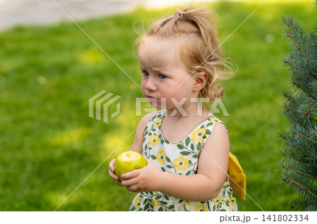 Serious Toddler Girl Holding Bitten Apple in Park Serious Toddler Girl Holding Bitten Apple in Park 141802334
