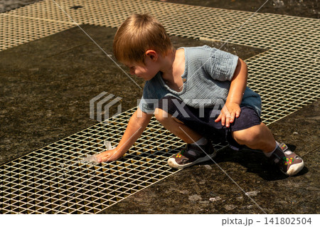 Young Boy Crouching to Touch Ground Fountain Jet 141802504