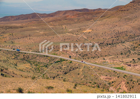 Desert highway with sparse vegetation, blue truck, and distant mountains 141802911