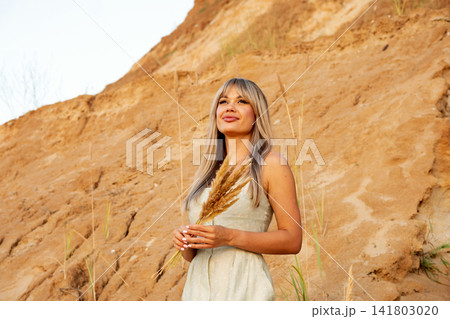 Woman Holding Dried Grass Bouquet Near Sandy Cliff Woman Holding Dried Grass Bouquet Near Sandy Cliff 141803020