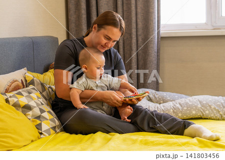 Baby Boy Touches Mother Chin During Playful Window Moment 141803456