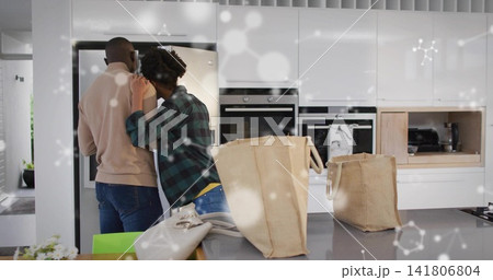 Unloading couple wearing tan sweater, plaid shirt placing totes and purse on island, copy space Unloading couple wearing tan sweater, plaid shirt placing totes and purse on island, copy space 141806804