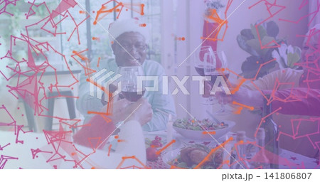 Smiling five senior adults raising wine glasses at dining table, one wearing Santa hat and sweater 141806807