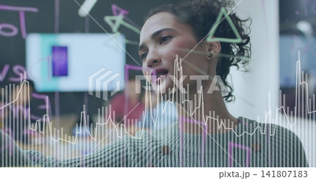 Writing woman sketching on glass board in office meeting with line-chart, wearing striped sweater Writing woman sketching on glass board in office meeting with line-chart, wearing striped sweater 141807183