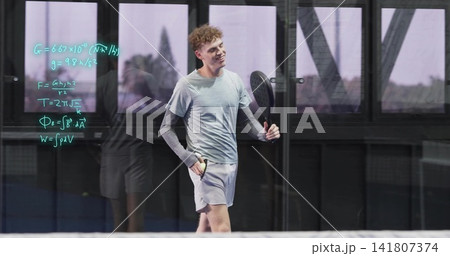 Smiling adult male in sportswear holding paddle, walking in glass court with teal equations and net Smiling adult male in sportswear holding paddle, walking in glass court with teal equations and net 141807374