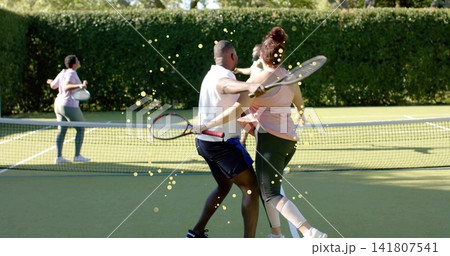 Hitting white-polo man and pink-top woman at tennis net on grass court, with rackets, balls, hedge Hitting white-polo man and pink-top woman at tennis net on grass court, with rackets, balls, hedge 141807541