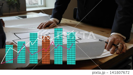 Leaning team in suits reviewing plans on table, holding pen, showing turquoise orange chart Leaning team in suits reviewing plans on table, holding pen, showing turquoise orange chart 141807672
