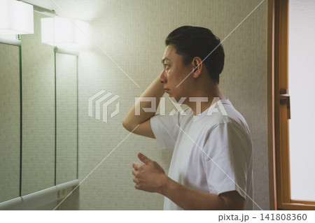 洗面台の鏡前で薄毛を気にしながら髪を整える40代男性のヘアチェック 141808360