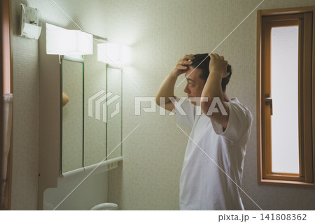 洗面台の鏡前で両手で髪のボリュームを確認する40代男性のヘアチェック 洗面台の鏡前で両手で髪のボリュームを確認する40代男性のヘアチェック 141808362