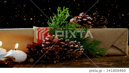 Showing wrapped kraft gift box red woven ribbon lace trim on rustic table, pinecones, lit candles 141808460