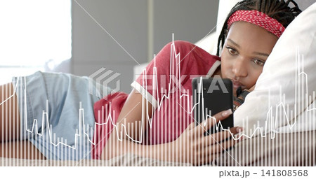 Reclining woman holding black phone in bedroom on bed wearing red tee white pillow waveform overlay 141808568