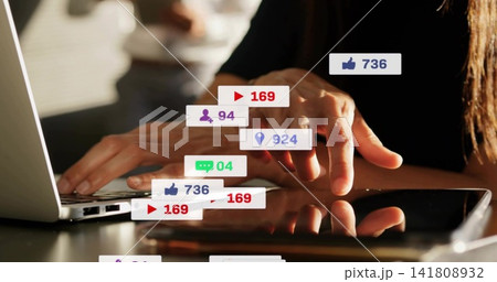 Tapping woman wearing black long-sleeve top using laptop and tablet at table with social overlays Tapping woman wearing black long-sleeve top using laptop and tablet at table with social overlays 141808932