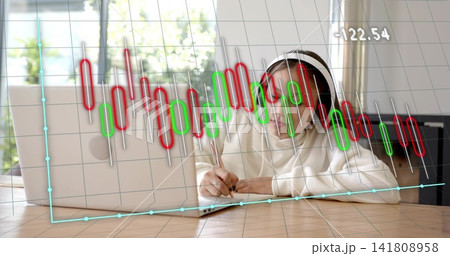 Studying girl in hijab pullover leaning at table with laptop notebook pen headphones chart -122 141808958