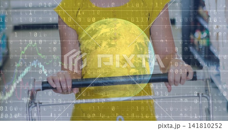 Standing shopper in yellow dress holding metal cart handle in supermarket aisle, with globe overlay 141810252