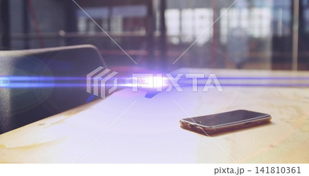 Resting smartphone on worn wood table in office, with long flare, windows, chair left, copy space 141810361