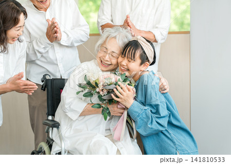 車椅子に乗るおばあちゃんに花束をプレゼントする笑顔の孫娘 車椅子に乗るおばあちゃんに花束をプレゼントする笑顔の孫娘 141810533