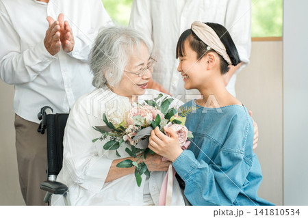 車椅子に乗るおばあちゃんに花束をプレゼントする笑顔の孫娘 車椅子に乗るおばあちゃんに花束をプレゼントする笑顔の孫娘 141810534