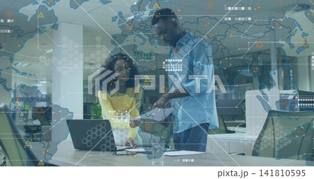 Standing pair checking laptop and papers at office meeting, yellow sweater, blue shirt, map overlay Standing pair checking laptop and papers at office meeting, yellow sweater, blue shirt, map overlay 141810595