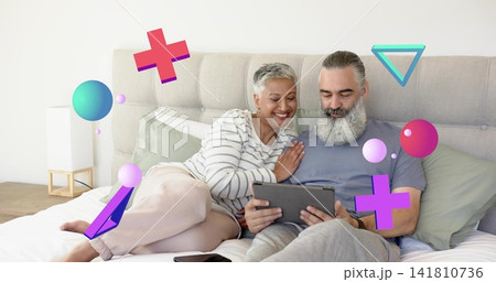 Reclining mature couple sharing tablet on bed in bedroom, man with beard, woman in striped top 141810736