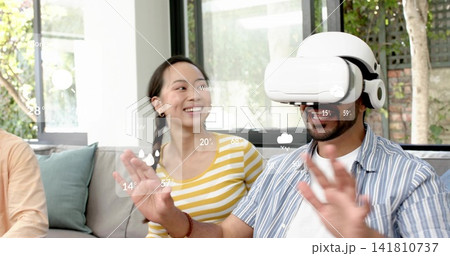 Reaching man with white VR headset gesturing on couch by windows, AR weather overlay, copy space 141810737