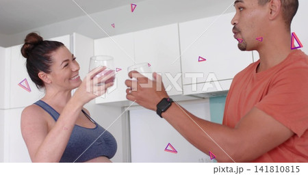 Toasting couple clinking clear glasses in kitchen wearing crop top orange tee watch pink overlays 141810815