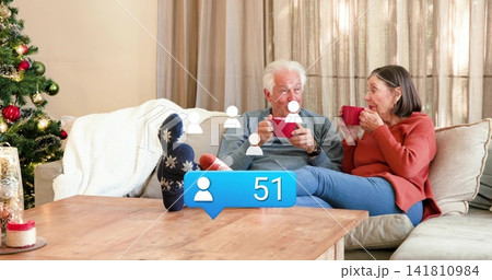 Chatting senior couple wearing casual-sweaters, sipping red-mugs on wooden table, showing bubble 51 141810984