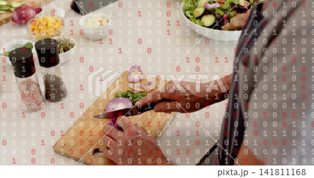 Cook slicing red onion on board in kitchen, with knife, herbs, in striped shirt, dark apron Cook slicing red onion on board in kitchen, with knife, herbs, in striped shirt, dark apron 141811168