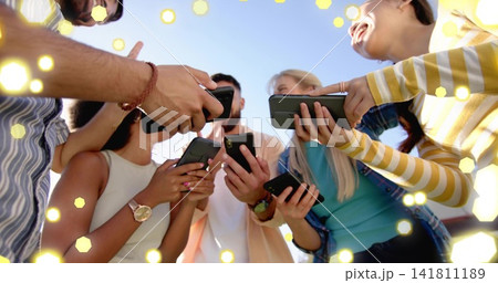 Holding smartphones, five friends leaning under blue sky, showing denim, watches and hex bokeh 141811189