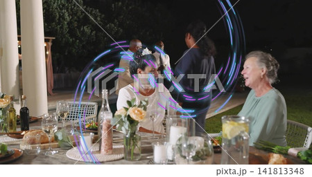 Talking seated woman in white blouse and floral hair clip at covered patio, with wine glasses 141813348