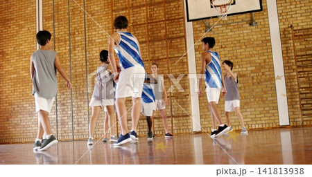 Playing students wearing blue-white jerseys and gray vests moving on school gym court, showing hoop Playing students wearing blue-white jerseys and gray vests moving on school gym court, showing hoop 141813938