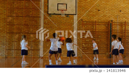 Playing group of seven children wearing white tees and navy shorts, practicing basketball near hoop Playing group of seven children wearing white tees and navy shorts, practicing basketball near hoop 141813946