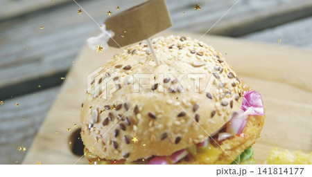 Showing seeded bun, sesame flax seeds, toothpick flag piercing patty, gold confetti on wooden board Showing seeded bun, sesame flax seeds, toothpick flag piercing patty, gold confetti on wooden board 141814177