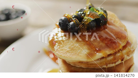 Pouring maple syrup over three pancakes on white plate in kitchen, blueberry bowl, mint, copy space Pouring maple syrup over three pancakes on white plate in kitchen, blueberry bowl, mint, copy space 141814270
