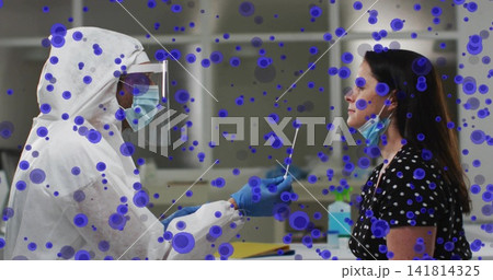 Giving clinician in PPE inserting nasal swab at clinic into patient in polka-dot top, purple spots Giving clinician in PPE inserting nasal swab at clinic into patient in polka-dot top, purple spots 141814325