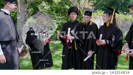 Standing grads in black gowns and caps on lawn holding red-ribbon diplomas, phone projecting globe 141814834