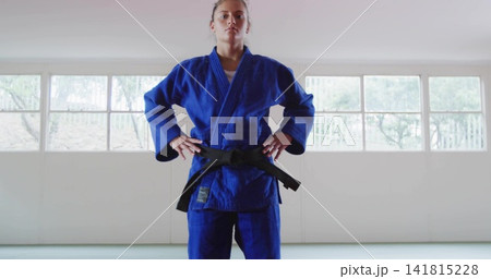 Standing female martial arts student holding focused stance in dojo, wearing blue gi and black belt Standing female martial arts student holding focused stance in dojo, wearing blue gi and black belt 141815228