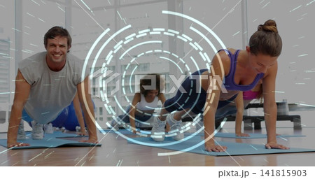 Holding group of five adults maintaining planks on blue mats in studio, wearing sportswear 141815903