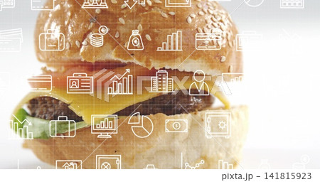 Displaying burger sitting on studio backdrop with sesame bun, melted cheddar, patty, finance icons Displaying burger sitting on studio backdrop with sesame bun, melted cheddar, patty, finance icons 141815923