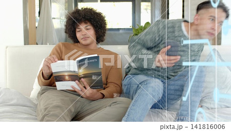 Reading man in brown sweater reclining on light sofa, holding Endless Sunsets near glass partition 141816006