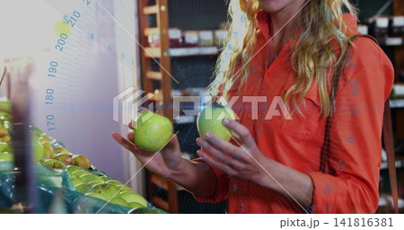 Choosing woman in orange-red shirt selecting fruit at grocery produce bin, holding two green apples Choosing woman in orange-red shirt selecting fruit at grocery produce bin, holding two green apples 141816381