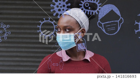 Standing adult woman wearing blue surgical mask, gray headscarf and maroon sweater at storefront Standing adult woman wearing blue surgical mask, gray headscarf and maroon sweater at storefront 141816693